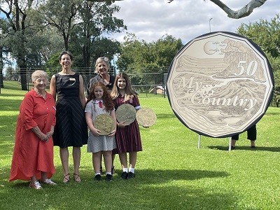 Gunnedah Shire representatives, school children and Mint Director standing with a large Dorothea Mackellar coin stand